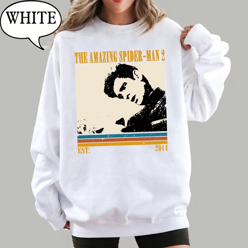 May include: White sweatshirt with a graphic from "The Amazing Spider-Man 2." The design features a black and beige image of a person, with text and stripes in orange, blue, and brown. The text "EST. 2014" is also included.
