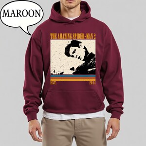 May include: Maroon hoodie with a graphic from "The Amazing Spider-Man 2" in a retro style. The design includes a black and white image, the film title, and the year 2014. The hoodie has a front pocket and a hood.