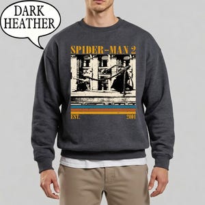 May include: Dark heather gray sweatshirt featuring a graphic from the movie Spider-Man 2. The design includes the movie title, a vintage-style image, and the year 2004. The sweatshirt has a crew neck and long sleeves.