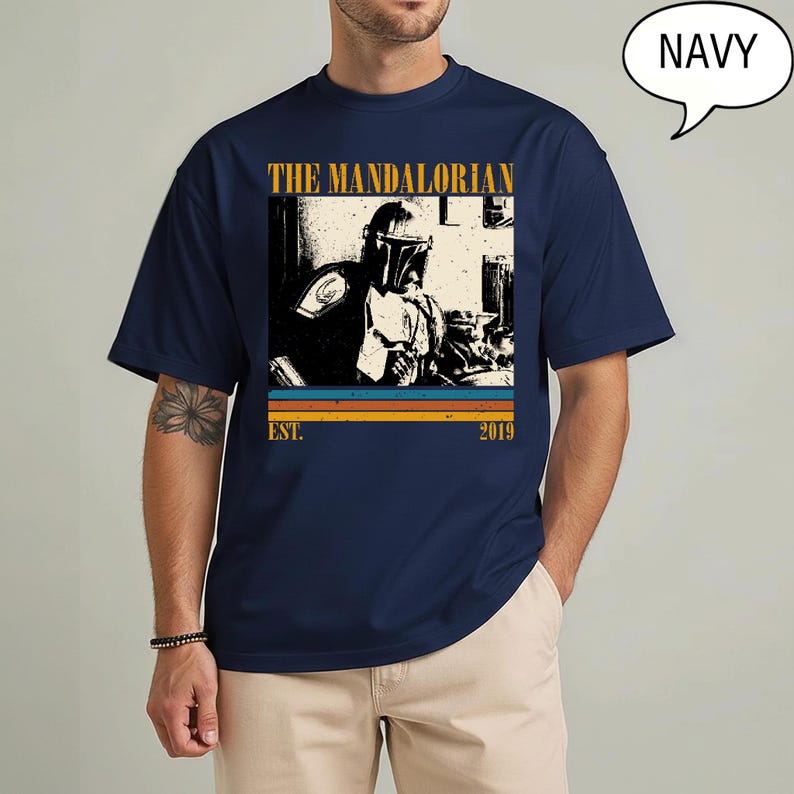 Może przedstawiać: Granatowa koszulka z nadrukiem The Mandalorian. Projekt zawiera złoty napis "THE MANDALORIAN" z napisem "EST. 2019" poniżej. Obraz ma wygląd vintage z poziomymi paskami w kolorze pomarańczowym, ż&oacute;łtym i niebieskim.