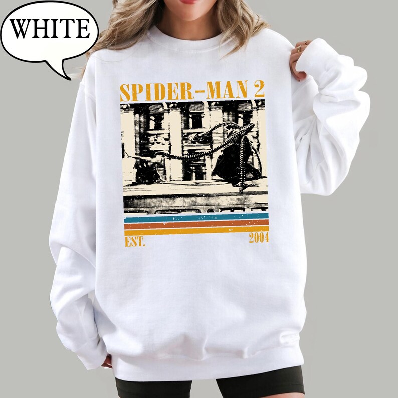 May include: White sweatshirt featuring a graphic from Spider-Man 2. The design includes the film's title, a vintage-style image, and the year 2004. The sweatshirt has a crew neck and long sleeves.