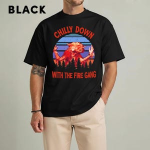 May include: Black t-shirt with the text "CHILLY DOWN WITH THE FIRE GANG" in red and orange. The graphic features a monster with orange fur and a blue and purple background. The word "BLACK" is at the top.