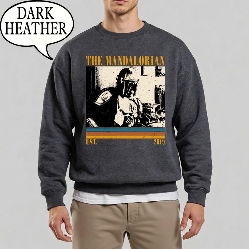 Może przedstawiać: Ciemnoszara bluza z nadrukiem The Mandalorian. Projekt zawiera napis "THE MANDALORIAN" nad wizerunkiem postaci, z napisem "EST. 2019" poniżej. Bluza ma okrągły dekolt.