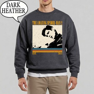 May include: Dark grey sweatshirt with a vintage-style graphic from "The Amazing Spider-Man 2". The design includes a black and white image of a person, the film title, and the year 2014.