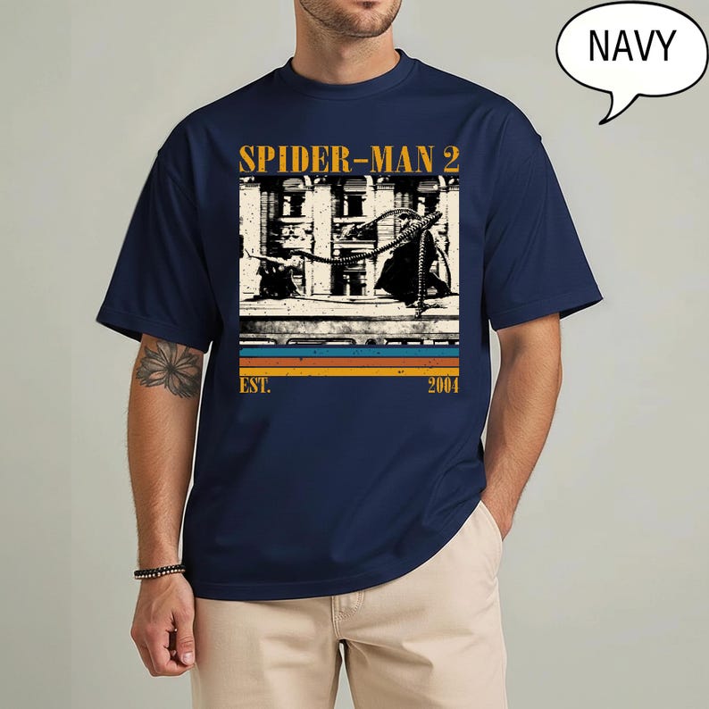 May include: Navy blue t-shirt featuring a graphic from Spider-Man 2. The design includes the text "SPIDER-MAN 2" in gold, a black and white image, and the text "EST. 2004" in a retro style.