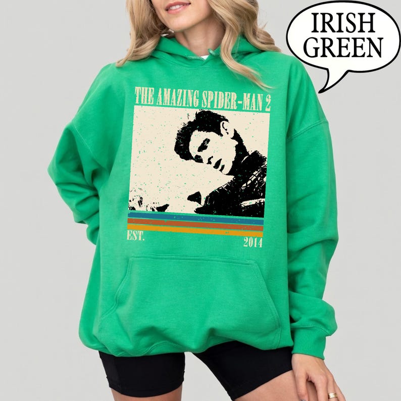May include: An Irish green hoodie with a graphic from "The Amazing Spider-Man 2". The design features a black and white image of a man, with text above reading "THE AMAZING SPIDER-MAN 2" and "EST. 2014" below. The hoodie is a pullover style.