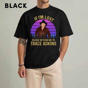 May include: Black t-shirt with a graphic featuring Trace Adkins. The design includes the text "IF I'M LOST PLEASE RETURN ME TO TRACE ADKINS" in gold lettering, set against a purple and blue sunset backdrop. The word "BLACK" is at the top.