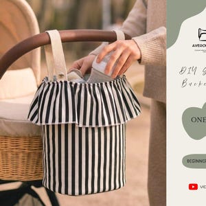 May include: A black and white striped stroller bucket bag with a frilled top, attached to a stroller. The bag is designed to hold baby essentials. The text "DIY Stroller Bucket Bag" and "One Size" are visible.