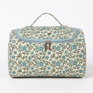 May include: A rectangular toiletry bag featuring a cream-colored base with a repeating pattern of small teal flowers and green leaves. The bag includes a top handle, a light blue zippered closure with two silver-toned metal pulls, and rounded corners.