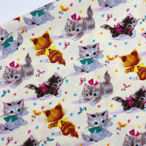 Peut inclure: Un tissu de couleur crème présentant un motif répétitif de chatons dans diverses positions. Les chatons sont représentés dans des tons gris, marron et orange, agrémentés de nœuds roses ou verts. De petits papillons et des fleurs étoilées sont dispersés.