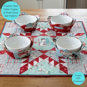 May include: A quilted table topper with a red, white, and blue snowflake pattern, featuring four white bowls in matching fabric bowl cozies. The cozies have holiday-themed text. The image includes the text "Feather Star Table Topper & Bowl Cozy Set Pattern."