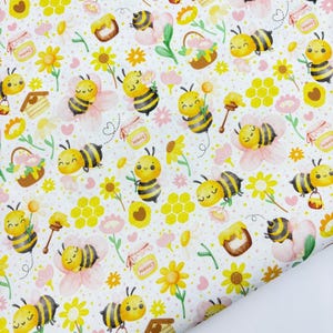 May include: A white fabric with a repeating pattern of cartoon bees, flowers, honey pots, and honeycomb. The bees are yellow and black, and the flowers are yellow and pink. Honey pots have the word "HONEY" on them.