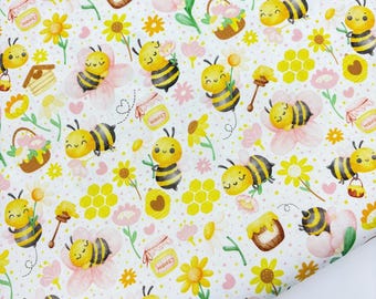 May include: A white fabric with a repeating pattern of cartoon bees, flowers, honey pots, and honeycomb. The bees are yellow and black, and the flowers are yellow and pink. Honey pots have the word "HONEY" on them.