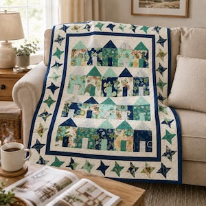 May include: A cozy quilt featuring a village design with houses in shades of blue, teal, and floral patterns. The quilt has a cream background with a navy blue border and star accents. The quilt is draped over a beige sofa.