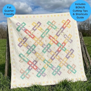 Puede incluir: Un edredón de color crema con un diseño geométrico de rectángulos entrelazados en colores pastel: verde, morado, amarillo y coral. El edredón se exhibe al aire libre e incluye el texto "Fat Quarter Friendly" y "Includes BONUS Cutting Tips & Shortcuts Guide".