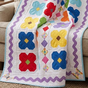 Puede incluir: Una colcha blanca con aplicaciones de flores de tela coloridas en rojo, azul, amarillo y azul claro. La colcha incluye un borde ondulado morado, detalles en forma de diamante y pequeñas piezas de tela con forma de mariposa en las esquinas.