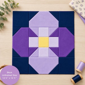 May include: A square quilt block featuring a central yellow square surrounded by light purple, medium purple, and dark navy blue fabric pieces. The block displays a geometric floral pattern and includes text stating the unfinished size is 12.5 x 12.5 inches.