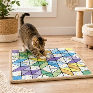 Op de afbeelding: Een rechthoekige krabmat voor katten met een geometrisch patroon in blauw, groen, geel en paars. Het heeft een natuurlijke vezelrand. Een tabby kat rekt zich uit op de mat.