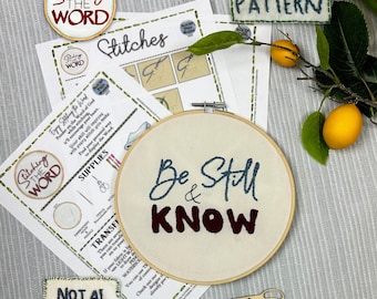 May include: An embroidery hoop containing white fabric with the blue and dark red stitched text Be Still & KNOW. Included are printed instruction sheets, a small stitched label reading NOT AI Handmade, and a small pair of gold scissors.