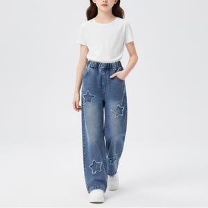 May include: A person wearing a white t-shirt and blue denim jeans. The jeans have a star-shaped design on the front. The person is wearing white sneakers.
