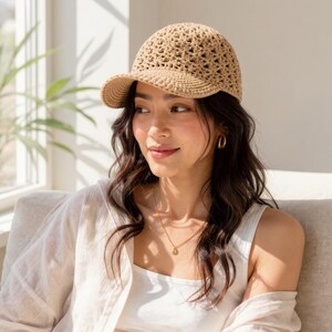 Peut inclure: Une casquette de baseball en crochet beige présentant un motif ajouré complexe sur la calotte et une visière solide aux mailles serrées. Le chapeau est fabriqué à partir d'un fil de couleur neutre, offrant un aspect texturé et artisanal.