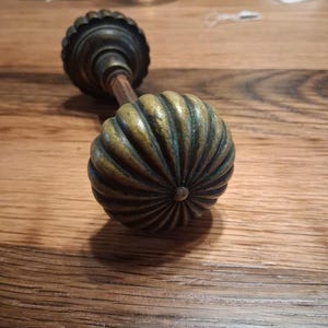 May include: Antique brass door knob with a ribbed, pumpkin-shaped design. The knob has a dark patina and is mounted on a wooden spindle. The hardware is likely vintage and adds a classic touch to any door.
