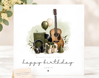 Puede incluir: Una tarjeta de cumpleaños cuadrada con una ilustración en acuarela de una guitarra acústica, auriculares negros, un disco de vinilo, un regalo y globos. El texto dice: WISHING YOU A VERY happy birthday JAMIE. Una pequeña tarjeta está colocada delante.