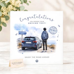 May include: A square greeting card featuring a watercolour illustration of a person standing behind a blue hatchback car. Text reads: Congratulations, You Passed Your Driving Test!, New Journeys Ahead, You Did It!, and Enjoy The Road Ahead.