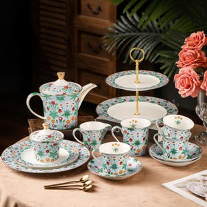 May include: A floral tea set including a teapot, cups, saucers, sugar bowl, creamer, and a two-tiered serving stand. The set has a light blue backdrop with a pattern of red, orange, and green flowers and leaves, with gold detailing.
