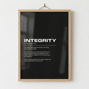 May include: A framed print with the definition of "INTEGRITY" in white text on a black background. The definition includes the pronunciation, the meaning, and the characteristics of a person with integrity. The frame is made of light-colored wood.