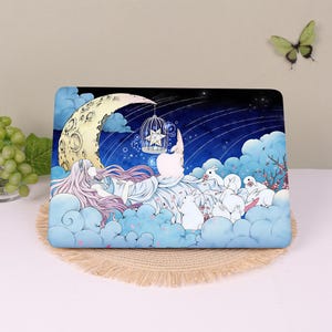 May include: A rectangular laptop skin featuring a fantasy illustration of a person with long pink hair resting on blue clouds under a crescent moon. A birdcage with a star hangs from the moon, surrounded by white rabbits and falling petals.
