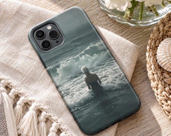 May include: A smartphone case featuring a monochromatic, grainy photographic print of a person standing in ocean waves. The case has a dark gray frame with a cutout for a triple-lens camera system on the upper left corner and a smooth finish.