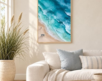 May include: A rectangular wall art print featuring an aerial view of a sandy beach meeting turquoise ocean waves. The scene includes small figures walking along the shoreline, captured in a light wooden frame with a clean, vertical orientation.