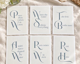 May include: Six rectangular art prints on a light beige background, each featuring dark blue serif typography. The prints display inspirational phrases including Peace often comes in waves, Where the water softens everything, Take less Breathe more, A quiet space shaped by water, Rest comes in waves, and Rest Here.