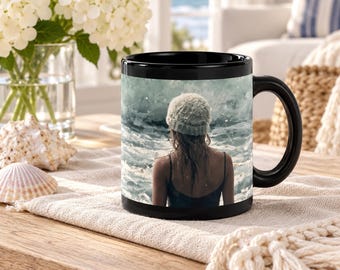 May include: A black ceramic mug featuring a photographic print of a person wearing a knit beanie and a dark tank top, standing with their back to the viewer while facing a turbulent ocean with crashing waves and sea foam.