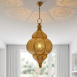 Pode incluir: Uma luminária pendente de metal em tom dourado com um padrão perfurado intrincado que projeta sombras circulares detalhadas no teto. A peça apresenta um formato bulboso de vários níveis suspenso por uma corrente e suporte a condizer.