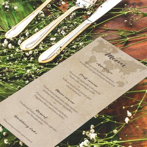 May include: A formal table setting with silverware, including a spoon, fork, and knife, with gold accents. The utensils are arranged on a wooden surface, decorated with greenery and a menu card.