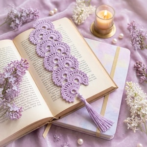 May include: A handmade, lavender crochet bookmark with a tassel, resting on an open book. The bookmark features a delicate, lacy design. The scene includes a lit candle, lilac flowers, and a notebook, creating a cozy, reading-themed aesthetic.