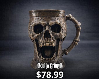 May include: A bronze-colored skull-shaped mug with a handle designed to look like a bone. The mug has a detailed, textured surface and the text "Oculto Gringo" is printed on the front.