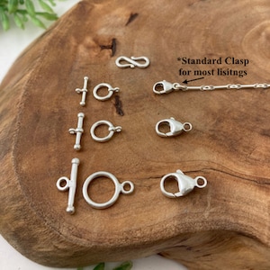 May include: A variety of silver clasps and jump rings for jewelry making. The clasps include a lobster claw clasp, a toggle clasp, and a figure eight clasp. The jump rings are different sizes. The text "*Standard Clasp for most listings" is visible in the image.