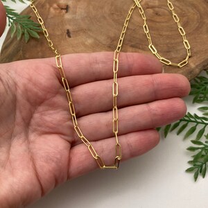 May include: A gold chain necklace with a delicate, linked design. The chain is made of small, oval-shaped links.