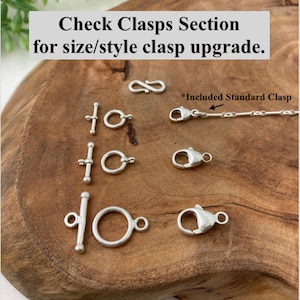 May include: A close-up of various silver clasps for jewelry, including a lobster clasp, a toggle clasp, and a ring clasp. The text "Check Clasps Section for size/style clasp upgrade." and "*Included Standard Clasp" are visible in the image.
