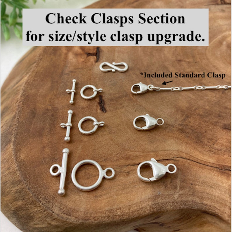 May include: A close-up of various silver clasps for jewelry, including a lobster clasp, a toggle clasp, and a ring clasp. The text "Check Clasps Section for size/style clasp upgrade." and "*Included Standard Clasp" are visible in the image.
