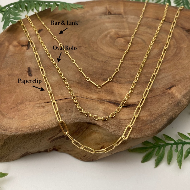 May include: Three gold chains on a wooden surface. The chains are labeled "Paperclip", "Oval Rolo", and "Bar & Link".