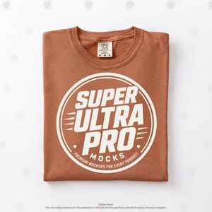 May include: A terracotta-colored crew neck t-shirt featuring a large white circular graphic on the chest. The graphic contains the text SUPER ULTRA PRO MOCKS and PREMIUM MOCKUPS FOR EVERY PRODUCT. A Comfort Colors brand label is visible at the neck.