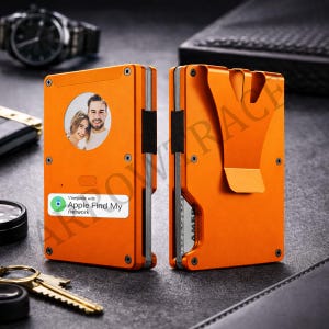 May include: Two bright orange metal wallets shown from front and back. The front features a circular photo of a couple and a white label with the text 'Compatible with Apple Find My network'. The back includes an integrated metal money clip.