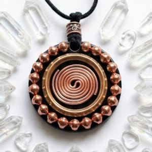 May include: A circular pendant on a black cord featuring a central copper wire spiral, a brass ring, and a border of small copper beads set against a black base. The pendant is surrounded by numerous clear, pointed quartz crystal shards.