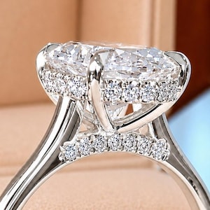 Peut inclure: Une bague argentée avec une grande pierre centrale de taille ovale maintenue par quatre griffes. Le panier et la partie supérieure de l'anneau sont ornés d'un pavé de petites pierres rondes et transparentes, offrant un aspect brillant et facetté.