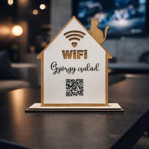 Op de afbeelding: Huisvormig houten WiFi-bord met een katten silhouet erop. Het bord toont het woord "WIFI", een familienaam en een QR-code. Het bord is gemaakt van lichtgekleurd hout en staat op een donkere ondergrond.