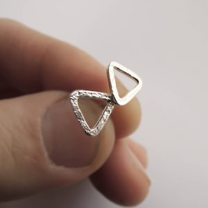 May include: A pair of silver triangle earrings with a textured finish. The earrings are connected by a small loop.